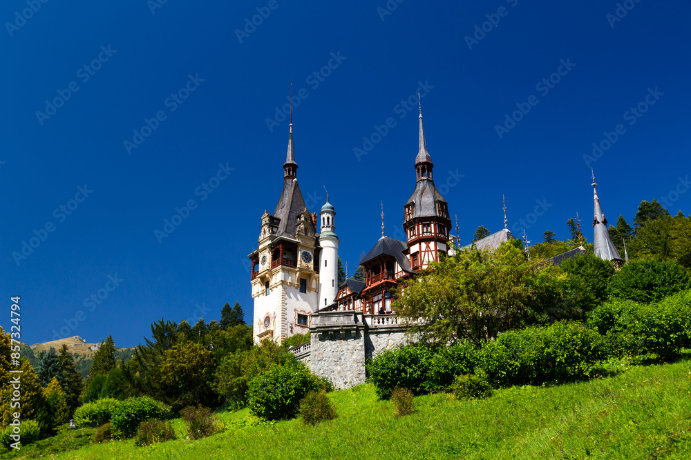 The Peles castle surrounded by splendid parklands in the town of Sinaia, Transylvania, Carpathian Mountains, Romania, Summer time, bright sunny day with dark blue sky. The Peles castle surrounded by splendid parklands in the town of Sinaia, Transylvania, Carpathian Mountains, Romania, Summer time, bright sunny day with dark blue sky.