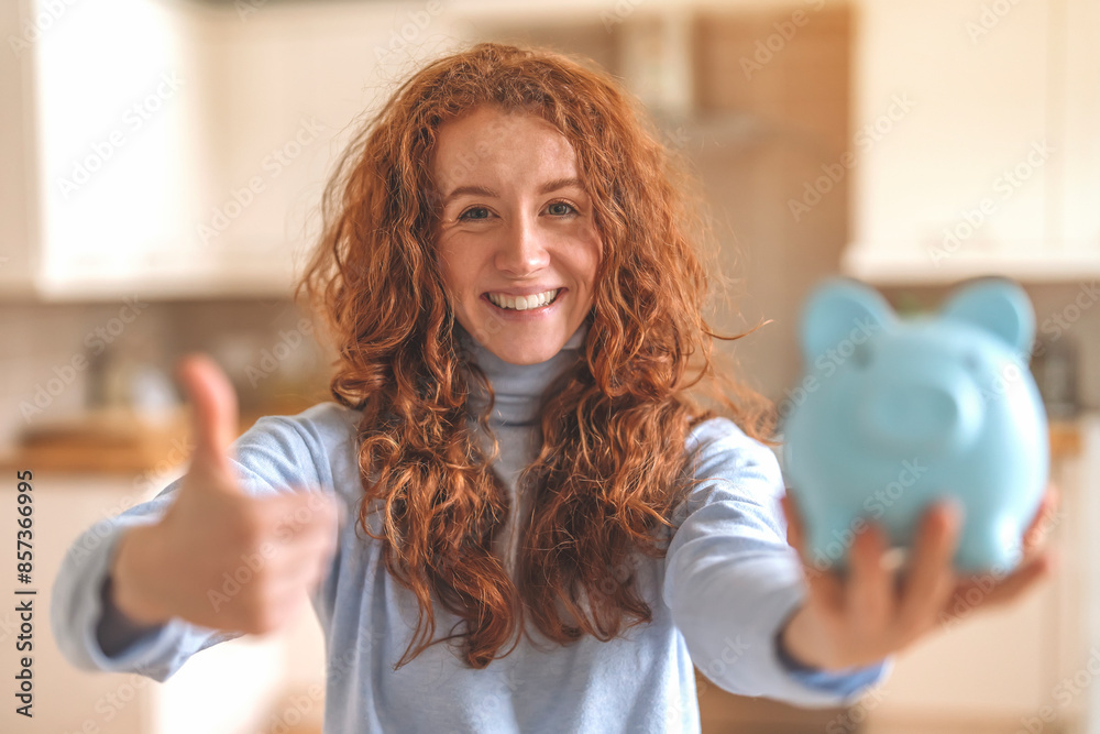 Smiling Woman Holding Piggy Bank and Giving Thumbs Up in Kitchen Smiling Woman Holding Piggy Bank and Giving Thumbs Up in Kitchen