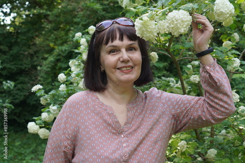 a traveler, an adult woman, holds round inflorescences with white flowers on the branches of viburnum of the Buldenezh variety in the botanical garden and natural park in summer while traveling photo