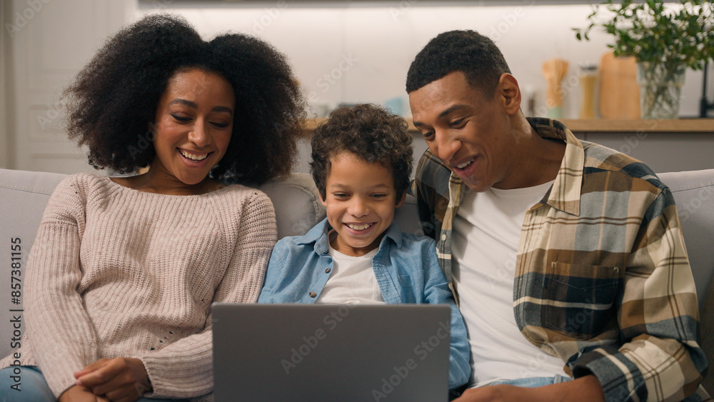 Happy African American family laughing woman mom female cheerful dad man male little boy son child kid watch movie cartoon using laptop computer pc playing game talking enjoy online shopping sofa home Happy African American family laughing woman mom female cheerful dad man male little boy son child kid watch movie cartoon using laptop computer pc playing game talking enjoy online shopping sofa home