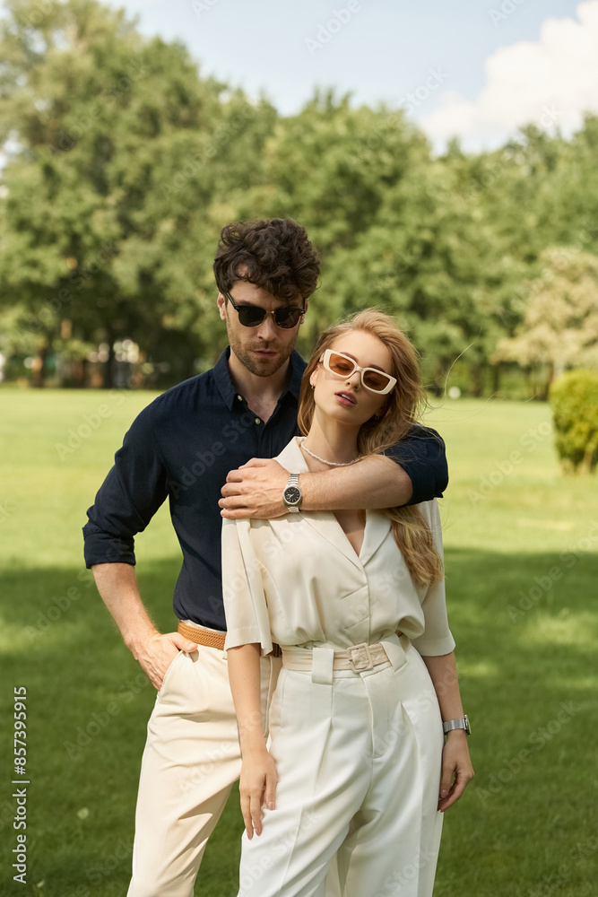 Elegant couple dressed in stylish attire posing outdoors in a park on lush green grass. Embracing the rich people lifestyle. Elegant couple dressed in stylish attire posing outdoors in a park on lush green grass. Embracing the rich people lifestyle.