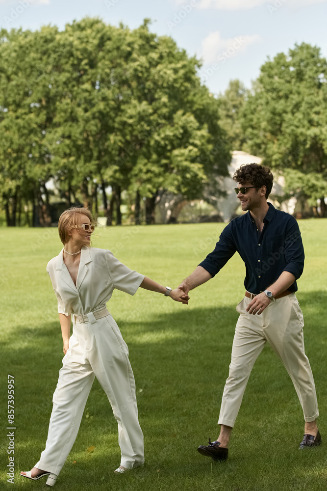 Obraz premium A stylish couple holds hands in a lush park, surrounded by greenery, embodying elegance and tranquility.