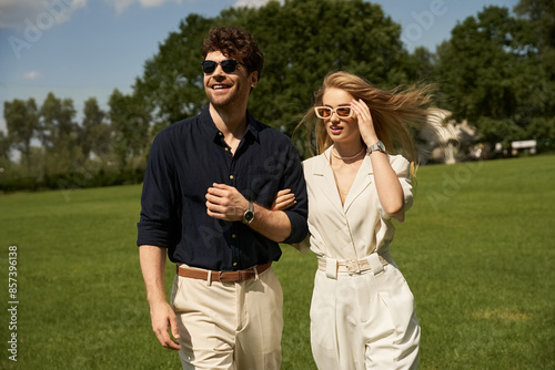 Foto A beautiful young couple in elegant clothing stroll through a lush green field in a display of old-money style and rich people lifestyle