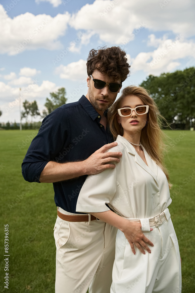 A beautiful young couple, dressed in elegant attire, poses affectionately in a lush green field under the vast sky. A beautiful young couple, dressed in elegant attire, poses affectionately in a lush green field under the vast sky.