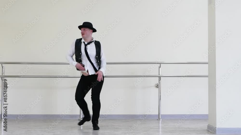 A cheerful and positive dancer twirls his tie. A jazzman in a hat creatively dances a street dance against the background of a wall