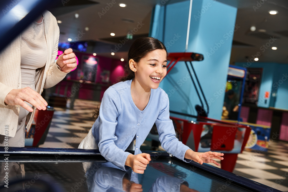 A mother and daughter enthusiastically play a game of air hockey, immersed in laughter and competitiveness at a mall gaming zone. A mother and daughter enthusiastically play a game of air hockey, immersed in laughter and competitiveness at a mall gaming zone.