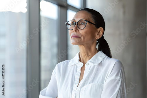 A woman wearing glasses and a white shirt is looking out the window