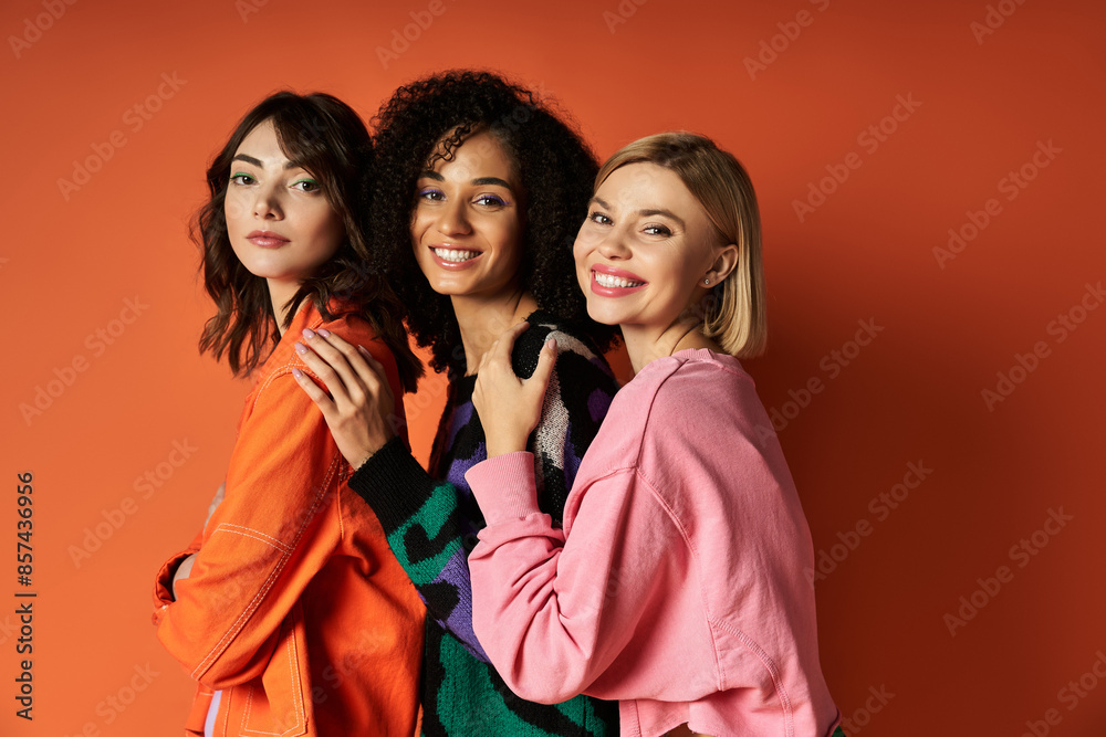 Young, beautiful multicultural women pose in stylish clothes on orange background, showcasing diversity and friendship. Young, beautiful multicultural women pose in stylish clothes on orange background, showcasing diversity and friendship.