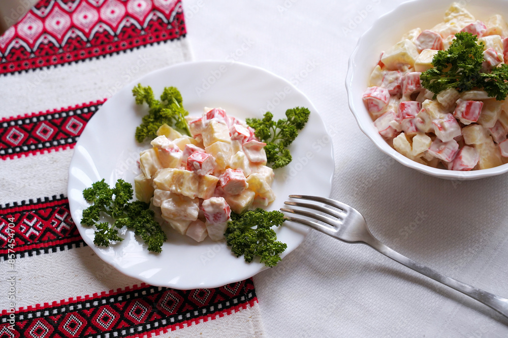 Homemade crab stick salad typical of modern Ukrainian cuisine and other Eastern European cuisines Traditional Ukrainian food on the table with embroidered tablecloth.