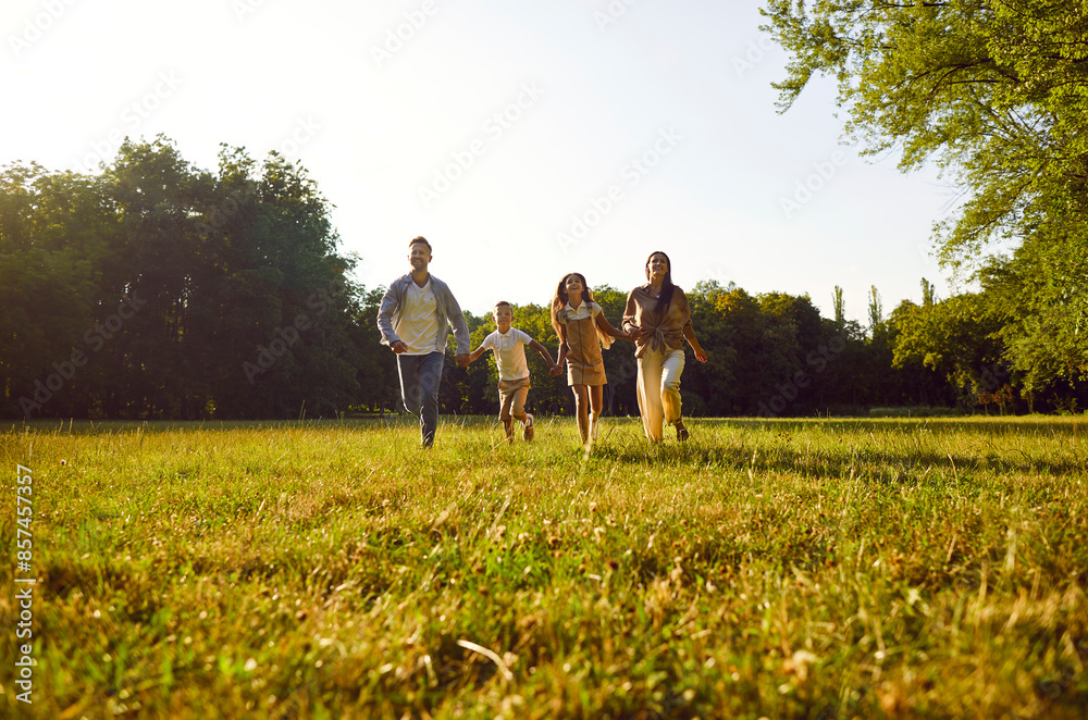 Happy smiling family with two kids boy and girl walking on green grass in summer park enjoying beautiful nature. Mother, father and their children running outdoors spending time together. Happy smiling family with two kids boy and girl walking on green grass in summer park enjoying beautiful nature. Mother, father and their children running outdoors spending time together.