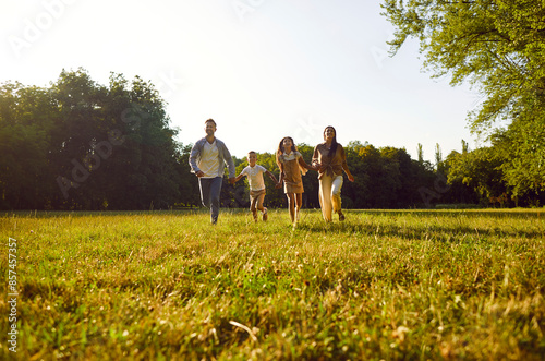 Happy smiling family with two kids boy and girl walking on green grass in summer park enjoying beautiful nature. Mother, father and their children running outdoors spending time together. © Studio Romantic