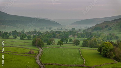 The soft light of dawn illuminates the peaceful meadow, showcasing the traditional stone walls and scattered farm buildings of Arncliffe in the Yorkshire Dales photo