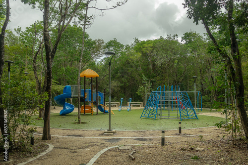 Colorful public children playground with fake green grass surrounded by tropical forest on a cloudy rainy day in Mexico