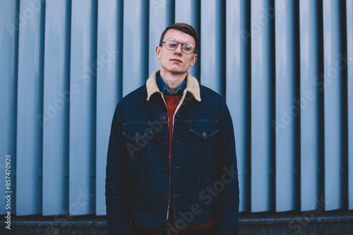 Half length portrait of stylish hipster bogger dressed in denim jacket posing on promotional background outdoors.Cool young man in design apparel looking at camera standing in urban setting