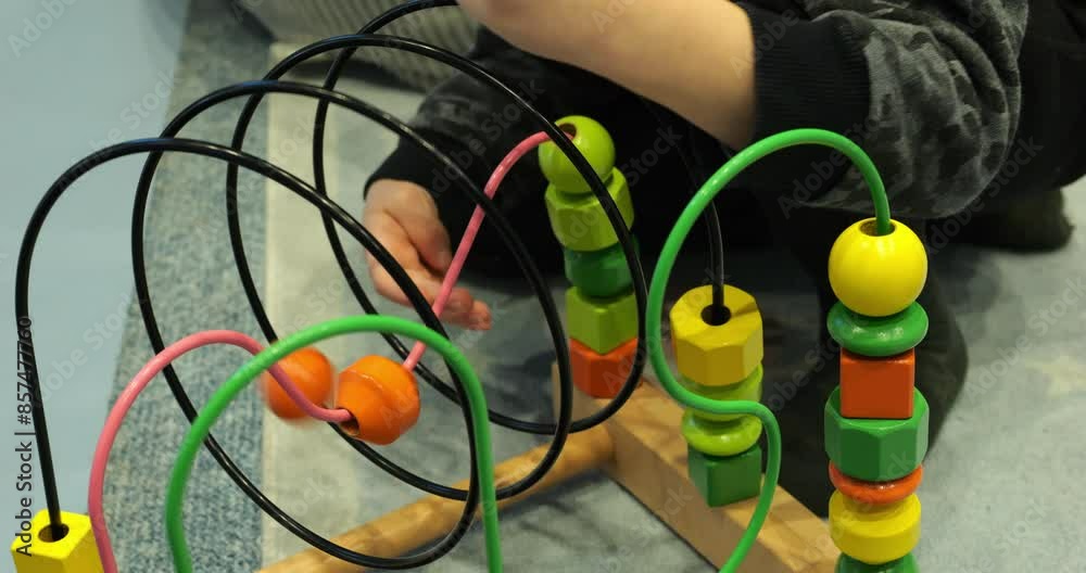 Little boy plays with colorful wire bead maze on floor closeup. Curious toddler child studies ball roller coaster in kindergarten. Children development Little boy plays with colorful wire bead maze on floor closeup. Curious toddler child studies ball roller coaster in kindergarten. Children development