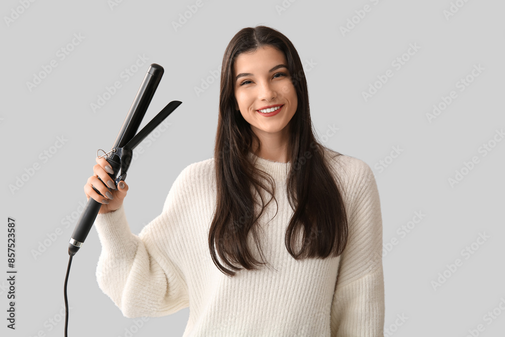 Beautiful young happy woman with curling iron on grey background Beautiful young happy woman with curling iron on grey background
