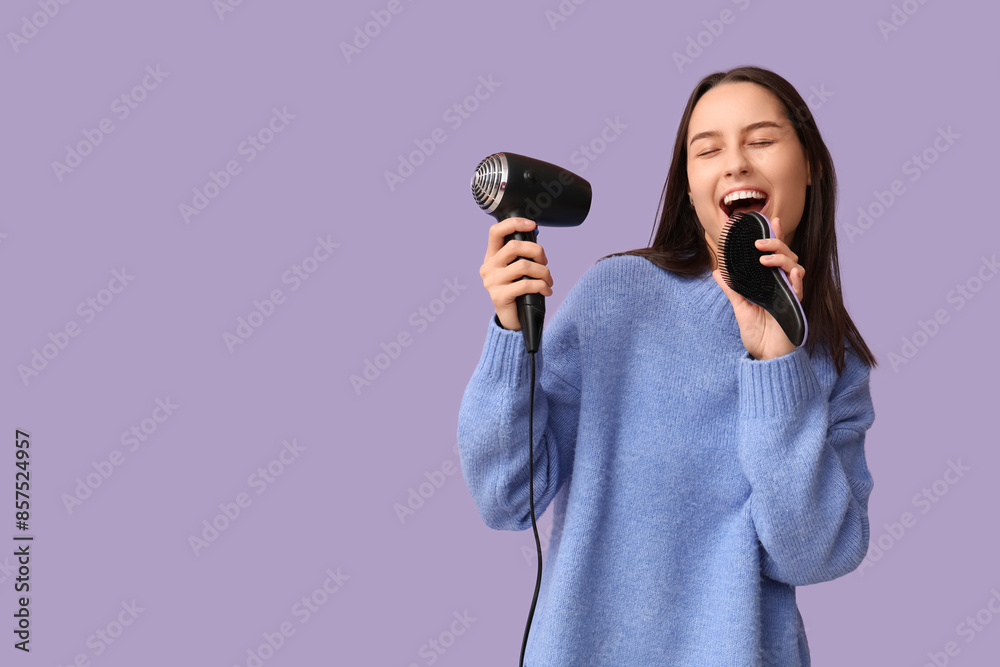 Singing young woman with hair dryer and brush on lilac background Singing young woman with hair dryer and brush on lilac background