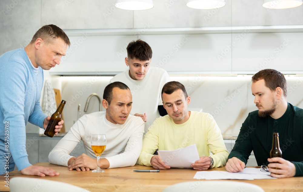 Fototapeta premium Man appearing upset as reading document, while friends gathering around, offering support and advices during friendly meeting at home kitchen..