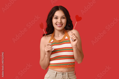 Happy young Asian woman with paper hearts on red background. Valentine's Day celebration