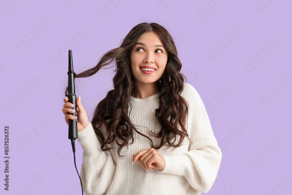 Young Asian woman curling hair on lilac background Young Asian woman curling hair on lilac background