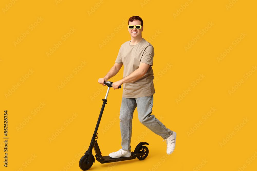 Young man riding modern electric kick scooter on yellow background Young man riding modern electric kick scooter on yellow background