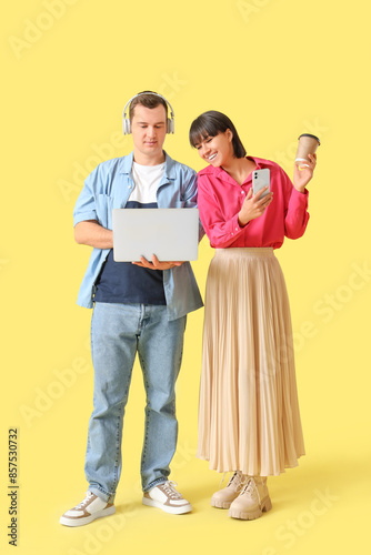 Young couple in love with gadgets and coffee cup on yellow background © Pixel-Shot