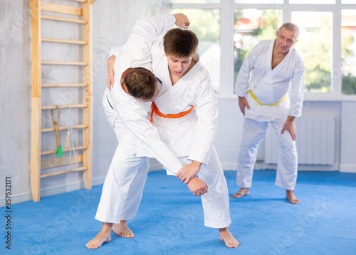 Adult man and young man in kimonos train judo techniques in studio