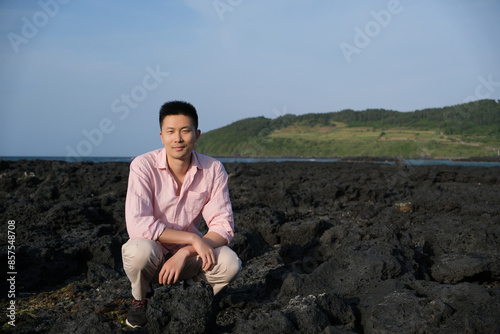 Asian male tourist squat at black basalt rocks at Hamdeok beach in Jeju island, South Korea photo