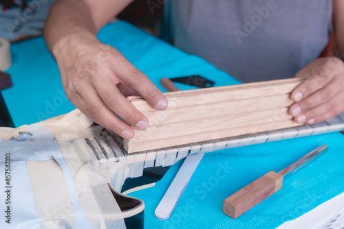 Fotografie Black electric guitar in repair shop with the hands of a guitar luthier fixing it, frets alignment