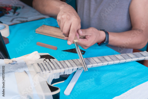 Obraz na plátně Black electric guitar in repair shop with the hands of a guitar luthier fixing it, frets alignment