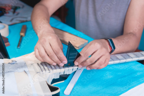 Obraz na plátně Black electric guitar in repair shop with the hands of a guitar luthier fixing it, frets alignment