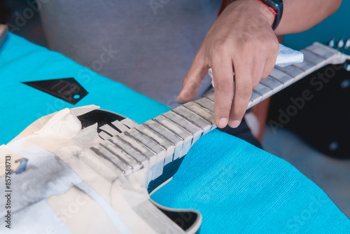 Obraz na plátně Black electric guitar in repair shop with the hands of a guitar luthier fixing it, frets alignment