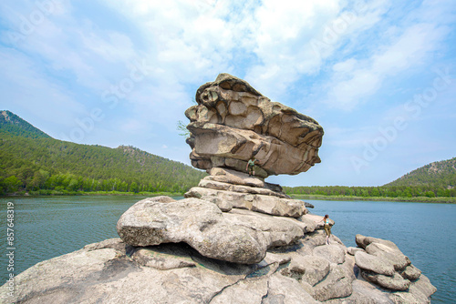 It is a Zhumbacktas rock. There are two people on it. There is green forest on the background. photo