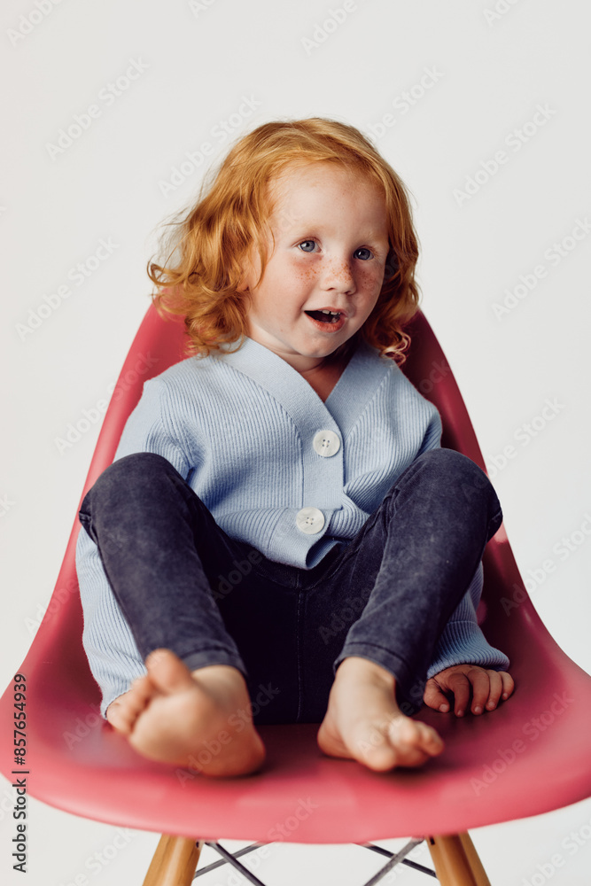 Little girl with red hair sitting on pink chair in front of white background beauty and innocence captured Little girl with red hair sitting on pink chair in front of white background beauty and innocence captured
