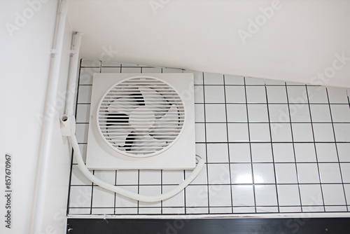 Plastic white exhaust fan mounted on a white tile wall in the kitchen.