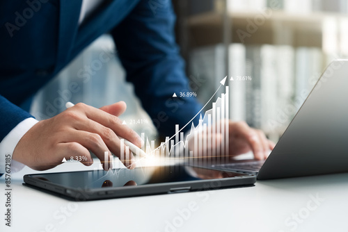 Businessman use laptop and tablet digital chart graphing company growth plan and up arrow, business graph growth Financial reports, economic charts Planning and strategy.
