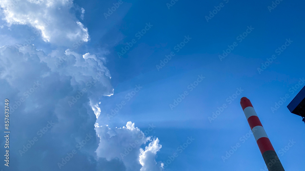The sky is filled with dramatic clouds and sunbeams, with a red and white striped pole standing tall against the clear blue background. The sky is filled with dramatic clouds and sunbeams, with a red and white striped pole standing tall against the clear blue background.