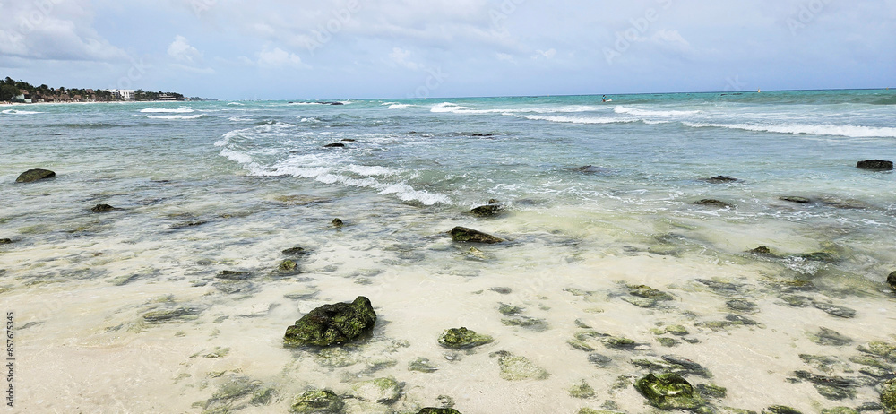 Fototapeta premium Beach and sea on a rainy day. Rocks covered in algae. Cloudy sky. Tides roll onto the beach. 