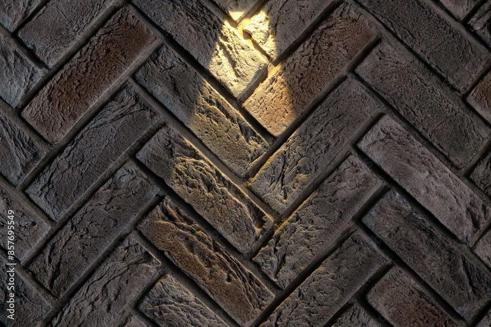 A fragment of a wall with decorative brick herringbone trim. A beam of light from a lamp falls on the textured surface. Background. A fragment of a wall with decorative brick herringbone trim. A beam of light from a lamp falls on the textured surface. Background.