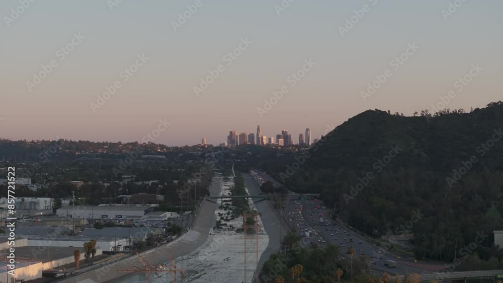 Aerial right to left above Los Angeles River with freeway and downtown skyline in background at golden hour. Aerial right to left above Los Angeles River with freeway and downtown skyline in background at golden hour.