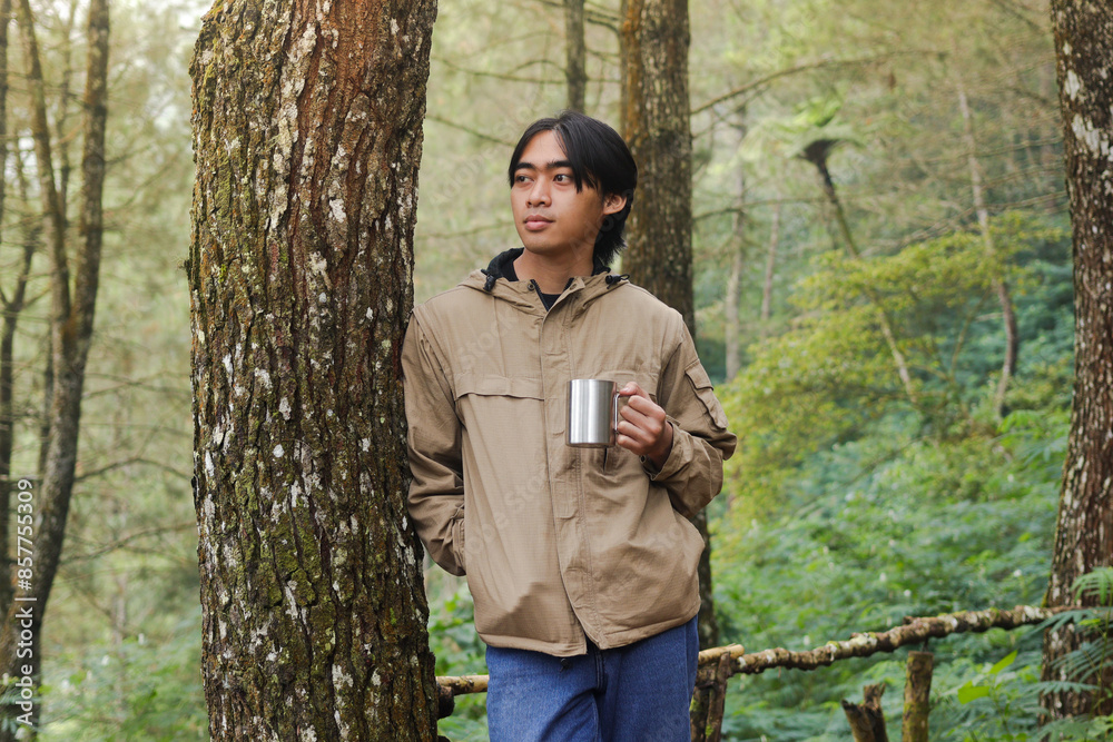Portrait of excited Asian hiker man drinking water from stainless steel cup while trekking in nature forest Portrait of excited Asian hiker man drinking water from stainless steel cup while trekking in nature forest