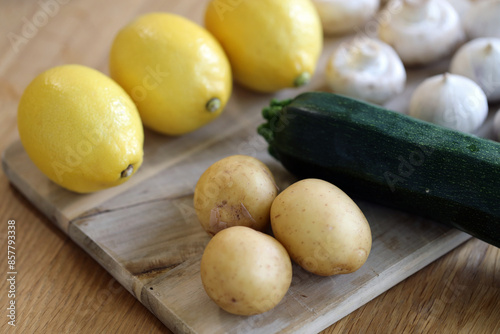 Scandinavian summer, fall season cuisine. Ingredients for a healthy meal: potatoes, garlic, zucchini and lemons on a wooden rustic cutting board. Fresh raw vegetables from season's harvest. Closeup.