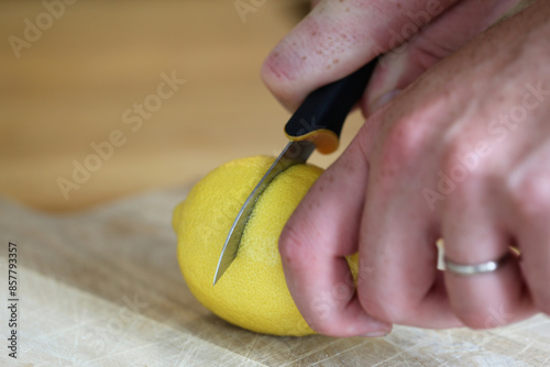 Cutting lemons - refreshing ingredient for cooking and baking. Closeup color image of the lemon, knife, cutting board and the hand of the man. Healthy lifestyle image.