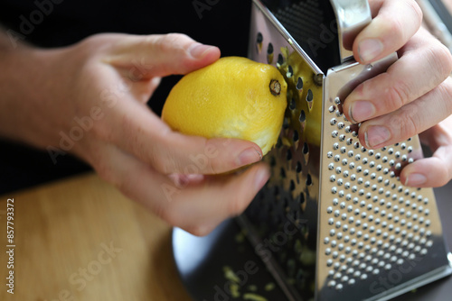 A white man grating lemon zest with a grater. Preparing food. Refreshing ingredients for cooking and baking. Closeup color image of the lemon, grater and the hand of the man. Healthy lifestyle image.