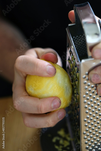 A white man grating lemon zest with a grater. Preparing food. Refreshing ingredients for cooking and baking. Closeup color image of the lemon, grater and the hand of the man. Healthy lifestyle image.