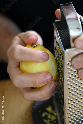A white man grating lemon zest with a grater. Preparing food. Refreshing ingredients for cooking and baking. Closeup color image of the lemon, grater and the hand of the man. Healthy lifestyle image.