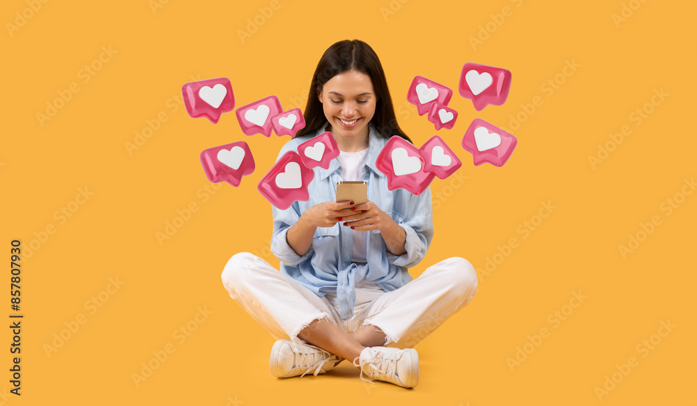 Young pretty woman in casual clothes using her phone, sitting cross-legged against a yellow background. Dating app Young pretty woman in casual clothes using her phone, sitting cross-legged against a yellow background. Dating app