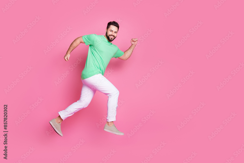 Full size photo of cheerful guy dressed green t-shirt white trousers running on at sale to empty space isolated on pink color background