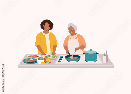 Smiling Black Elderly Mother In Apron Cooking Steak With Frying Pan. Adult Daughter Helping Her Mom To Cut The Cucumber. Half Length.