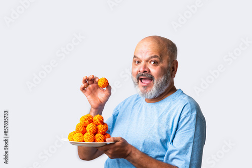 Indian asian senior old elderly man eating sweet bundi laddu or laddoo eating sweet bundi laddu or Boondi Laddoo photo